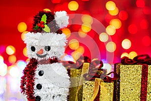 Snowman Christmas figurine near glittery gifts isolated on blurred background of lights. Christmas decorations isolated