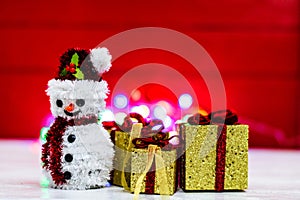 Snowman Christmas figurine near glittery gifts isolated on blurred background of lights. Christmas decorations isolated