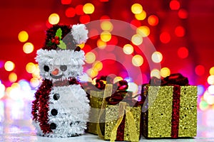 Snowman Christmas figurine near glittery gifts isolated on blurred background of lights. Christmas decorations isolated