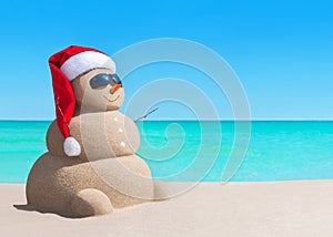 Snowman in Christmas Santa hat and sunglasses at sea beach