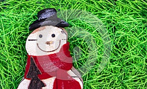 Snowman in a hat and scarf on a background of green shavings.