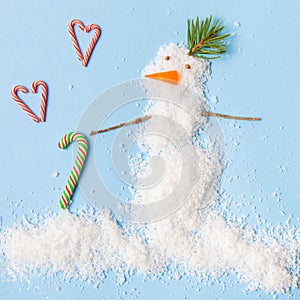 Snowman made of artificial snow on a blue background. Caramel hearts. New Year card