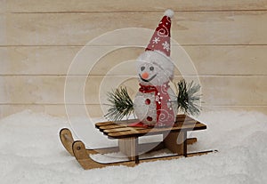 Snowman in a red cap with wooden sleigh