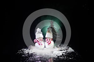 Snowman and Snow Woman with Heart on snow in dark background. New Year and Christmas conceptual image with fir tree. Sweet Snowman