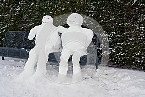 Snowman and snowwoman on a park bench in Winter
