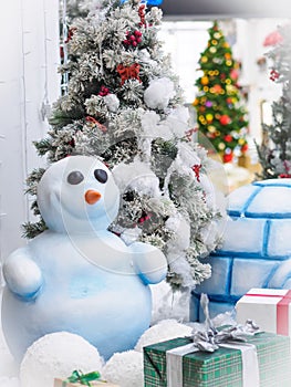 A snowman standing against Christmas trees surrounded with gift boxes.