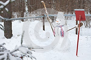 The snowman stands in the snow with a broom and a shovel