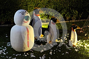 A snowman and three evil penguins are standing on a green lawn. Snowman with a green nose. Christmas celebration in countries with