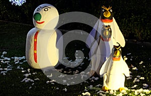 A snowman and three evil penguins are standing on a green lawn. Snowman with a green nose. Christmas celebration in countries with