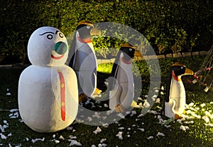 A snowman and three evil penguins are standing on a green lawn. Snowman with a green nose. Christmas celebration in countries with