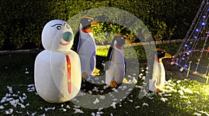 A snowman and three evil penguins are standing on a green lawn. Snowman with a green nose. Christmas celebration in countries with