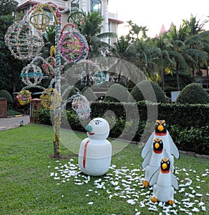 Snowman and three penguins on a green lawn, garden sculpture, palm trees and decorative trees