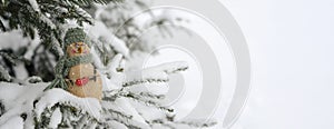 Snowman, toy on the background of a snowy Christmas tree. Snowing. Selective focus, blurred winter background. The