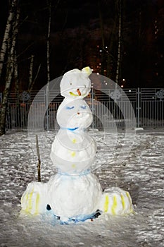 Snowman in winter evening courtyard lit by photo