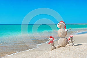 Snowmans family at sea beach in santa hat.