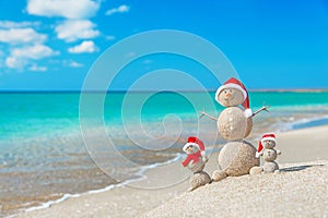 Snowmans family at sea beach in santa hat.