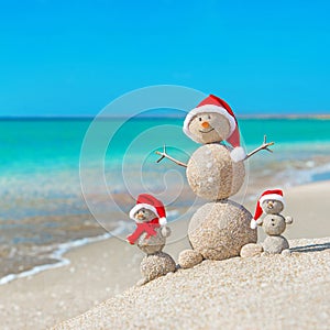 Snowmans family at sea beach in santa hat.