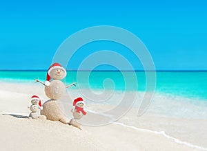 Snowmen family at tropical beach in santa hats. New Years and Ch