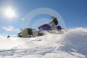 Snowmobile rider jumping machine on sunny hillside