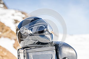 Snowmobile safety helmet lays at the luggage trunk mounted on backside of blue snowmobile, close up view. Blurry mountains covered