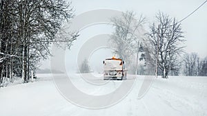 Snowplow highway maintenenace truck cleaning road completely white from snow in winter, dangerous driving conditions, view from
