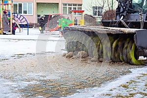 A snowplow removes snow from the sidewalk in the courtyard of a residential building