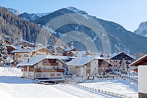 Snowy alpine village in Italy illuminated by sun with mountains in the background