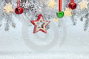 Snowy background with christmas tree branch, wooden decorative star, jingle bells and garland lights