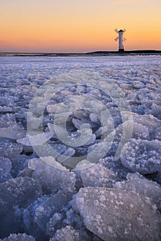 Snowy Baltic sea scene. Beautiful sunset over a windmill-shaped lighthouse. Swinoujscie, Poland.