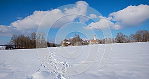 Snowy bavarian winter landscape with traditional church, blue sky with clouds