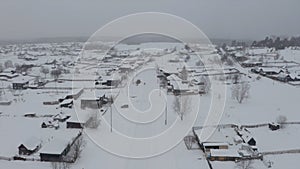 Snowy bird's-eye view. Clip. A white village in the snow with small wooden houses and next to it a large forest with