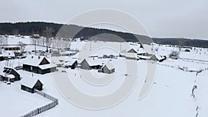 Snowy bird's-eye view. Clip. A white village in the snow with small wooden houses and next to it a large forest with