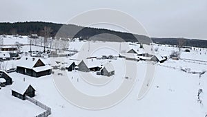 Snowy bird's-eye view. Clip. A white village in the snow with small wooden houses and next to it a large forest with