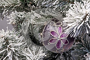 Snowy branch of christmas tree with fabric christmas violet-gray  ball with flower and glitter decorations close up