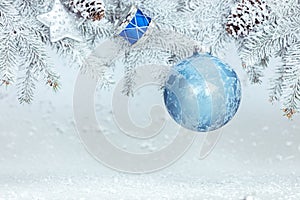 Snowy christmas background with fir tree branch decorated with blue ball, drum toy and star