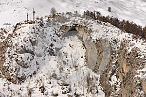 Snowy cliff with cave and sparse trees