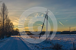 Snowy country lane by a field and village at sunset