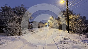 Snowy country road at evening time. Street lamp illuminating snow trail at winter night. Beautiful nature landscape with