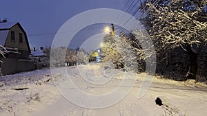 Snowy country road at evening time. Street lamp illuminating snow trail at winter night. Beautiful nature landscape with