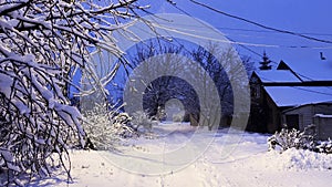 Snowy country road at evening time. Street lamp illuminating snow trail at winter night. Beautiful nature landscape with