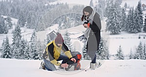 In a snowy day two tourist arrived in amazing place in mountain with a snowy forest on the background they have a break