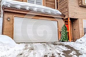 Snowy driveway in front of garage door and christmas tree by the front door