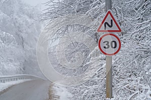 Snowy driveway and road sign speed limit 30 km. Winter forest after snowfall. Bad weather, fall.