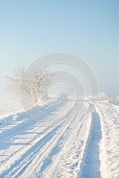 Snowy empty shoveled countryside road on a foggy winter morning at sunrise