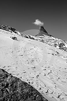 Snowy field with frozen snow and peak of the mountain looking like a chimney against the clear sky with cloud behind it photo