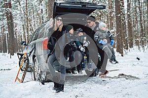 Snowy forest and caucasian family posing on car trunk in daytime