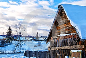 Snowy hills in Russian countryside in morning, red wooden house windows turned to east photo