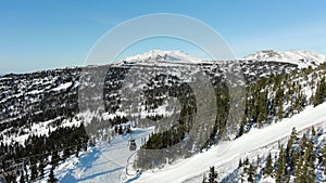 Snowy mountain hill with ski lift and forest under blue sky