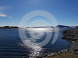 Snowy mountain peaks in early spring with clear blue sky and sunshine reflection on fjord surface