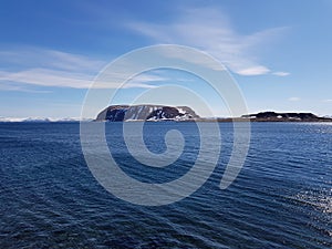 Snowy mountain peaks in early spring with clear blue sky and sunshine reflection on fjord surface